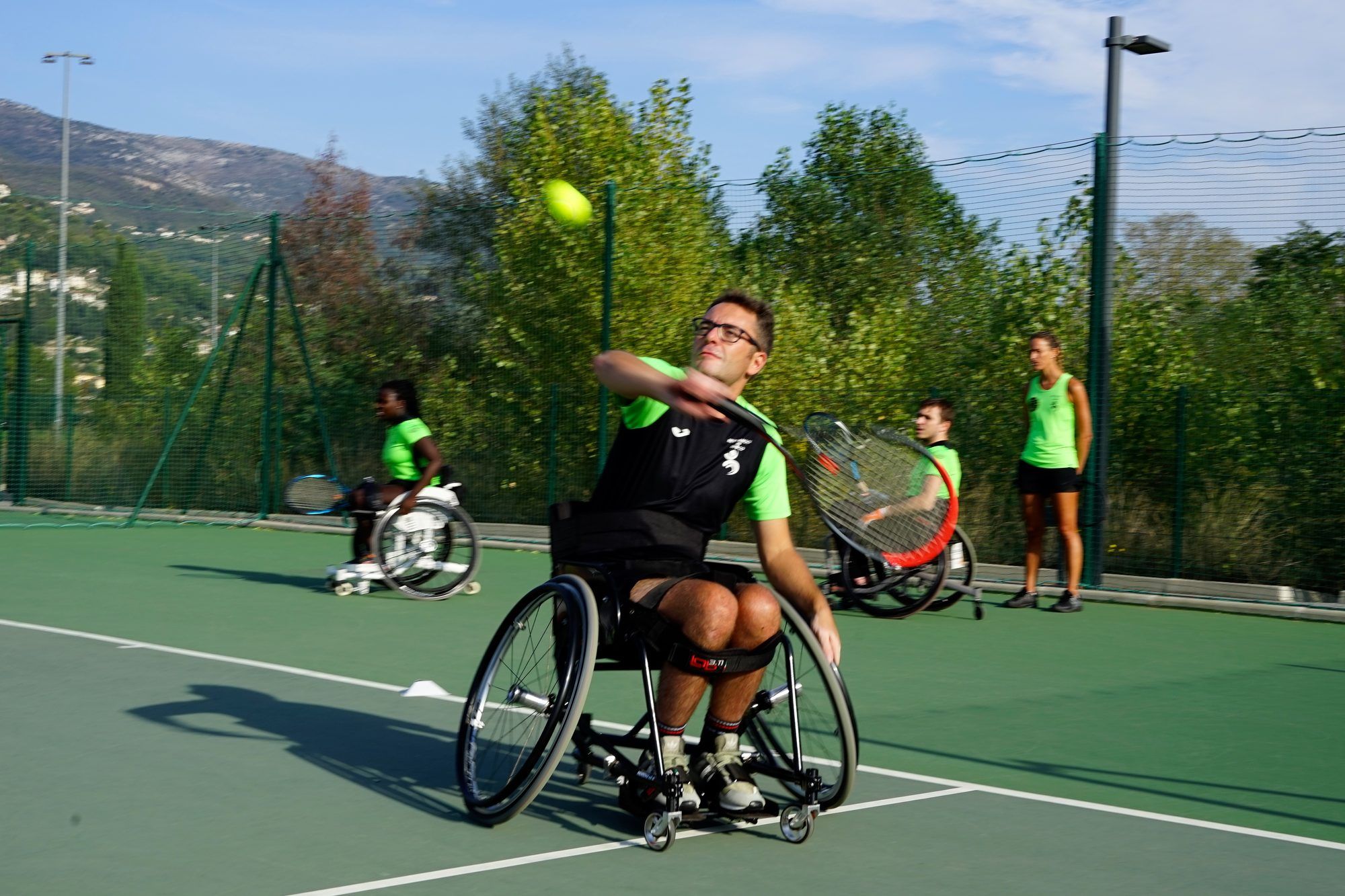 Tennista in carrozzina colpisce di dritto su un campo all’aperto, con le montagne sullo sfondo.